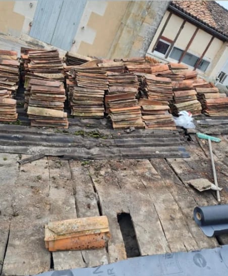Stacked old clay roof tiles piled against residential buildings with deteriorated wooden roof structure visible