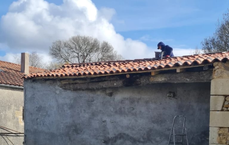 Person on terracotta tile roof of weathered stone building against blue sky with white clouds