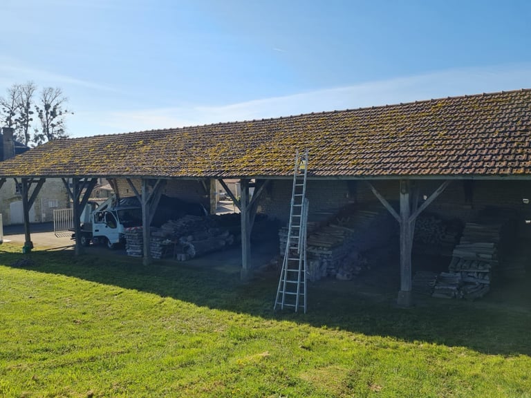 Large wooden barn with tiled roof, open-sided shelter containing farm equipment