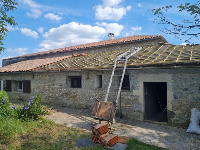 Stone cottage under renovation with new roof shingles, ladder against wall