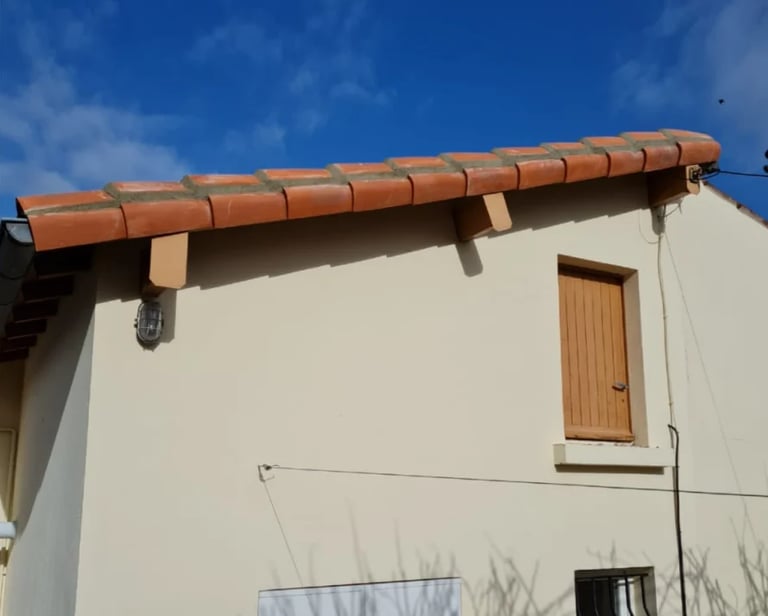 Terracotta roof gutter and drain pipe on a white building exterior against blue sky