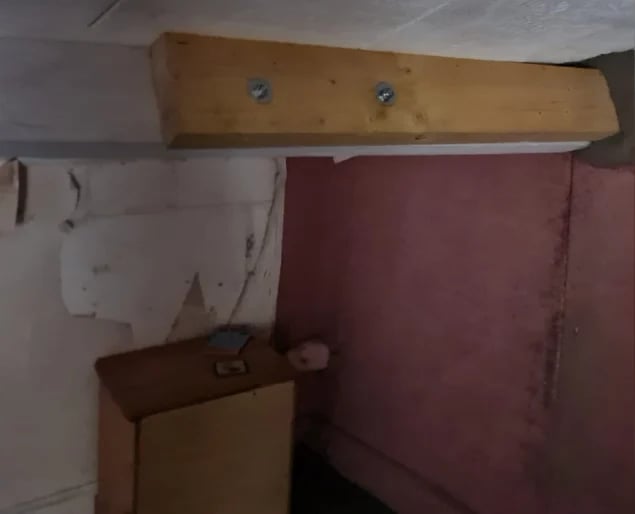 Interior corner showing wooden beam mounted on wall above burgundy fabric panel and worn white surface