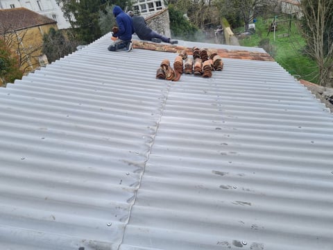 Worker installing terra cotta roof tiles on a corrugated metal roof