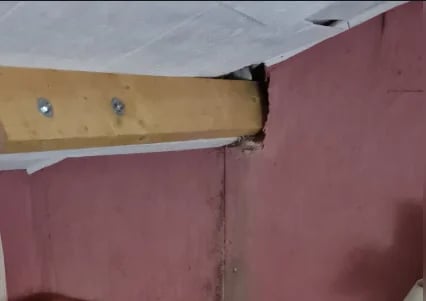 Wooden beam mounted on pink wall with metal brackets and fasteners visible at corner junction