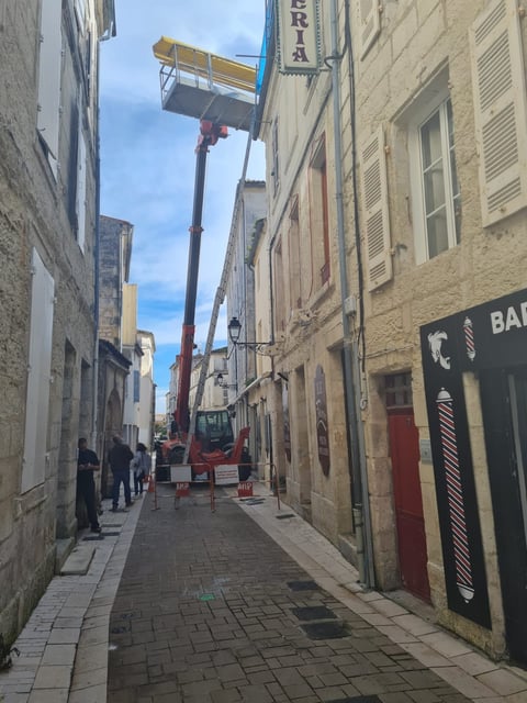 Red and yellow cherry picker lift elevated on narrow European street