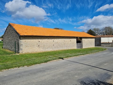 Stone barn with golden roof and dark slate gable, situated on green lawn