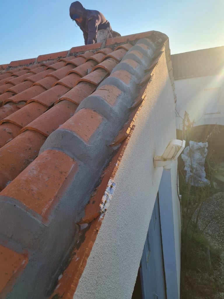 Worker installing metal roof flashing on terracotta tile roof during sunset