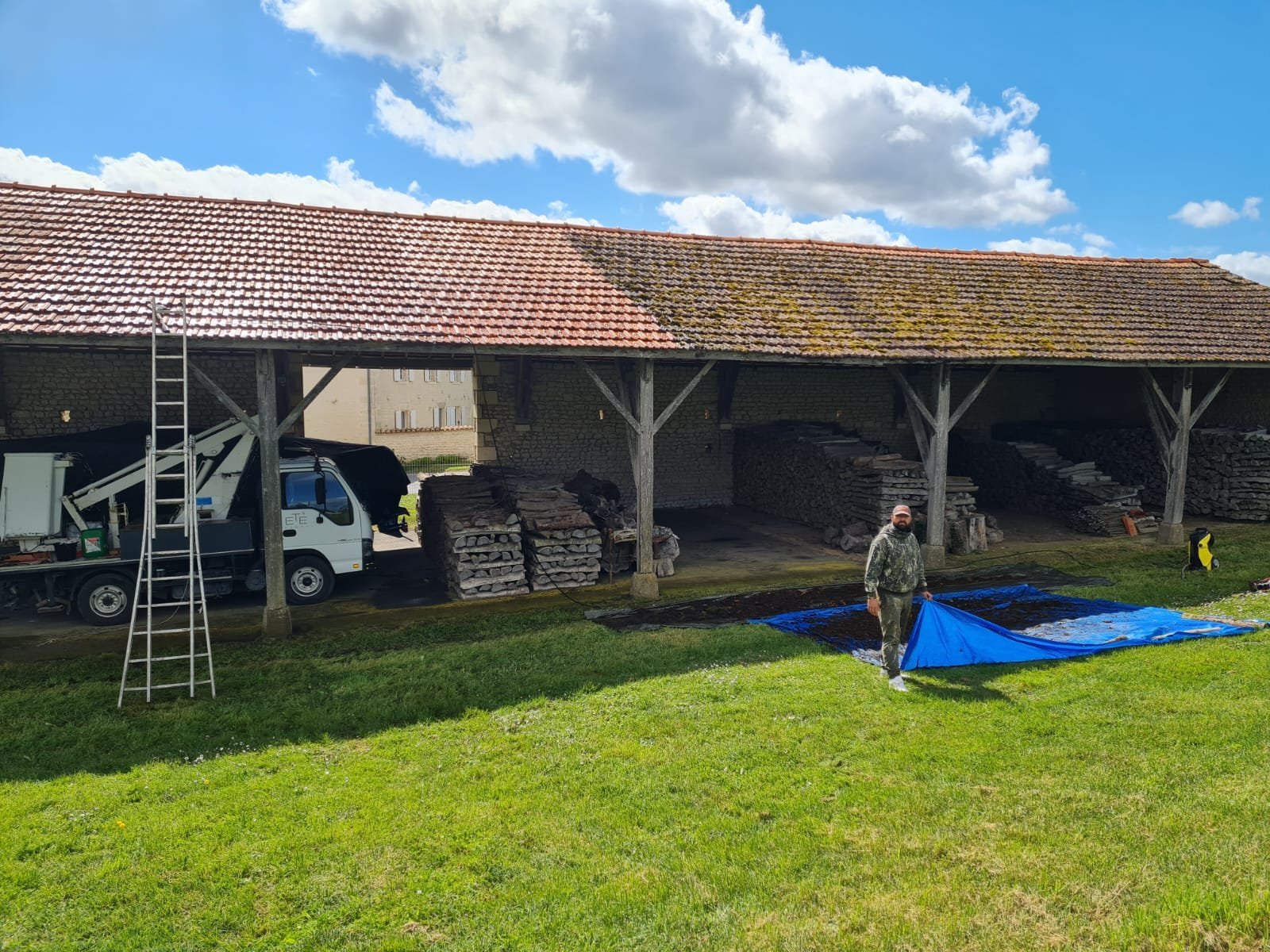 Workers with blue tarp at stone barn with white van and ladder during roof maintenance